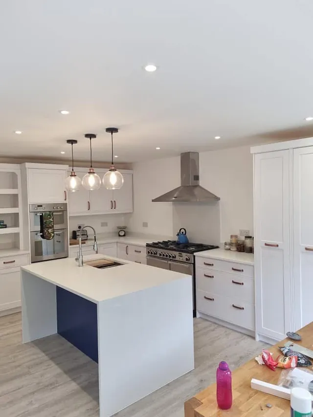 White kitchen with triple pendant lights over an island and downlights